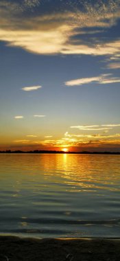 Güneşin gökyüzünü ve suyu altın ve turuncu tonlarda boyadığı büyüleyici bir günbatımı.