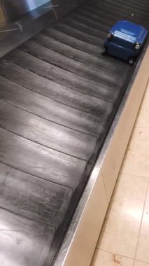 Havaalanı varış salonundaki bagaj atlıkarıncasında ilerleyen mavi sert bavulun yakın çekimi.