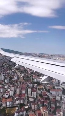 Bir uçak penceresinden çekilen hava görüntüleri, aşağıdaki şehir manzarasına karşı beyaz bir kanadın parçalarını gösteriyor.