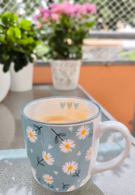 Balkonda cam sehpanın üzerinde aromatik kahve tezgahlarıyla dolu papatya desenli seramik bardak.