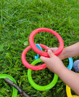 Parlak renkli plastik halkaları tutan ve onları güneşli bir günde yeşil çimenlere bağlayan çocukların ellerini kapatın.