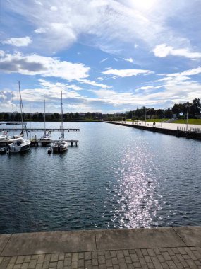 Bitterfeld, Almanya - 01.2025 Ağustos: Güneşli bir günde yat iskelesi, su parıldıyor, güneş ışınlarını yansıtıyor. Rıhtımda demirli yatlar ve tekneler huzur içinde sallanıyor. Güneş tarafından aydınlatılan set, sizi yürüyüşe davet ediyor.