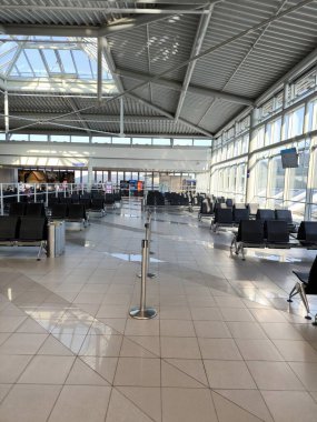 Leipzig, Almanya - 13 Ağustos 2025: güneşli, ferah ve boş bir havaalanı bekleme odası. Uzağa uzanan siyah sandalyeler sessizlik ve beklenti hissini vurgular..