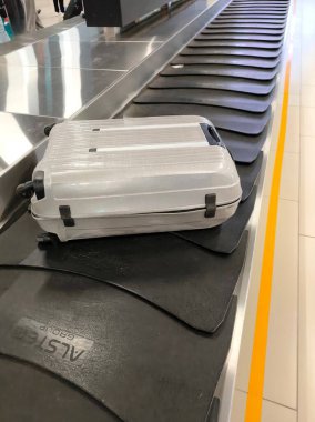 Havaalanındaki bagaj atlıkarıncasında hareket eden bir bavul. Çekim, tipik bir bekleyiş ve seyahat atmosferinin taşınması ve bagajların taşınması sürecine odaklanıyor..