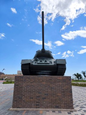 The Soviet T-34 tank monument stands on a tall, massive pedestal. The tanks gun is raised. A bright, clear blue sky occupies the background.