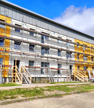 The facade of this modern multi-story residential building is completely covered in metal scaffolding. Major renovations, renovations, and insulation of the exterior walls are underway.