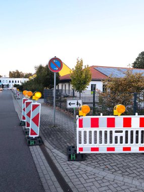 Construction work on a city street. A row of red and white road barriers and signal lights, as well as a round 
