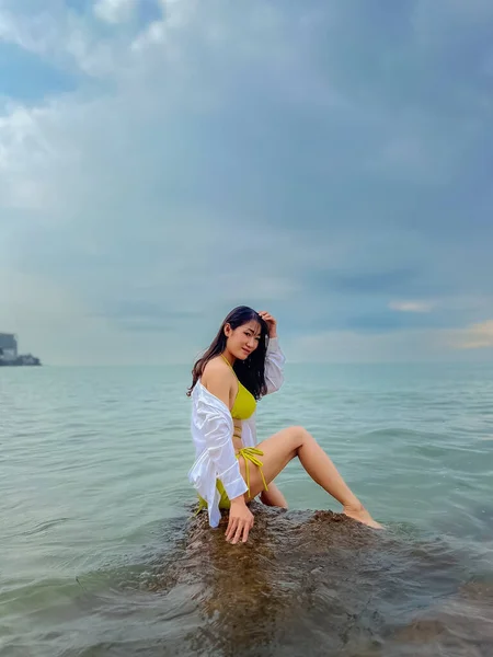 セクシーなアジアの女性黄色のボディスーツを身に着けている 海の中の岩の上に座り — ストック写真