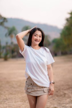 Güzel gülümseyen Taylandlı kız beyaz bir tişört ve halka açık bir parkta şirin bir etek giyiyor..