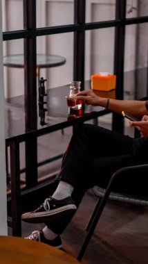 Genç adam evdeki sandalyede otururken kahve içiyor.