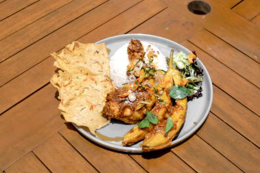 Kızarmış tavuğun yüksek açılı görüntüsü ahşap bir tabakta kızarmış patatesle birlikte siyah bir yüzeyi var.