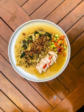 Beyaz tabakta tavuk ve sebzeli erişte çorbası.