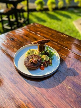 Ahşap bir masada, bir tabak soslu lezzetli bir bifteğin yakın plan çekimi.