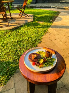 Baharatlı ve sebzeli ızgara tavuk eti akşam vakti bir arka bahçede ahşap bir masada.