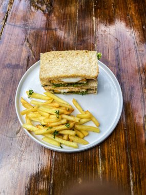 Beyaz tabakta kızarmış patates ve salatalı bir sandviçin yüksek açılı görüntüsü.