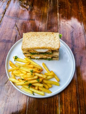 Patates kızartmalı sandviç ve ahşap tabakta taze sebze.