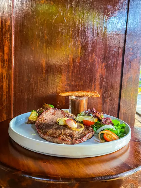 Ahşap masada sebzeli ızgara biftek.