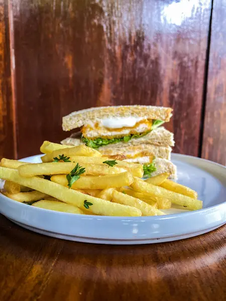 Tahta bir masada peynirli ve sahanda yumurtalı sandviçin dikey görüntüsü.