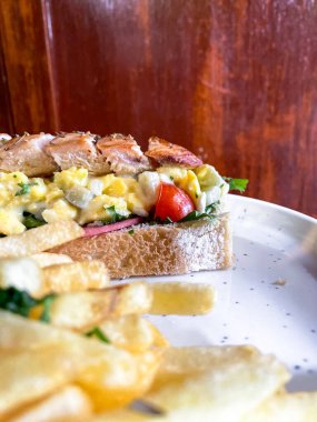 Tahta tabakta patates kızartması ve peynirli lezzetli ve taze sandviçin yüksek açılı yakın plan çekimi.