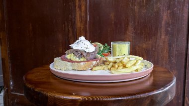 Tabakta hamburger, patates kızartması, sos ve salata.