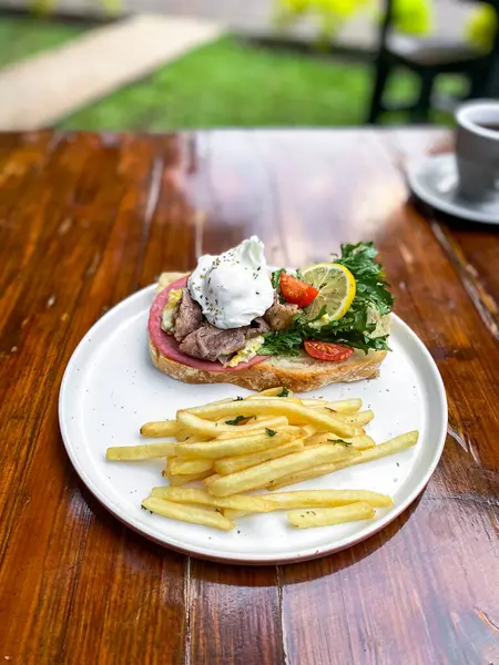 Sığır etli sandviç, patates kızartması ve ahşap masada taze salata.