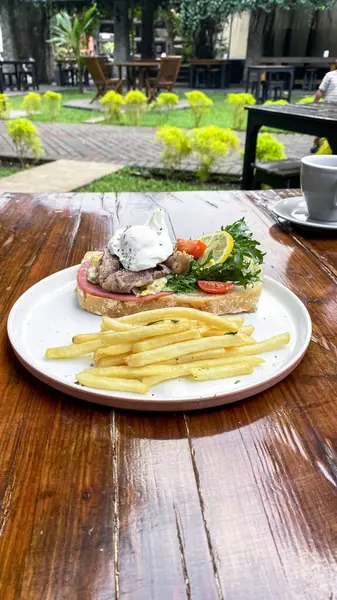 Tavada kızarmış yumurta, pastırma, domates, marul ve peynirli bir sandviç.