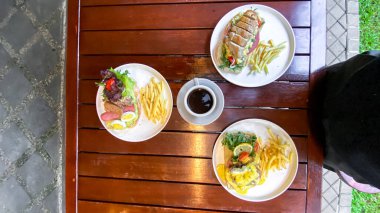 Tahta bir masada çatalla ızgara bifteğin dikey görüntüsü.