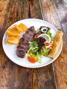 Tabakta biftek ve tahta masada salata. en üstteki görünüm