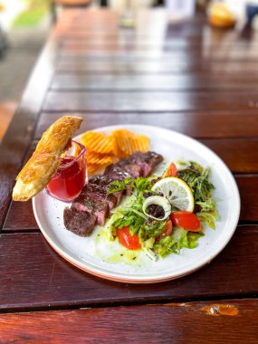 Sebzeli lezzetli bir bifteğin yüksek açılı çekimi ve ahşap bir masada beyaz bir tabakta et.