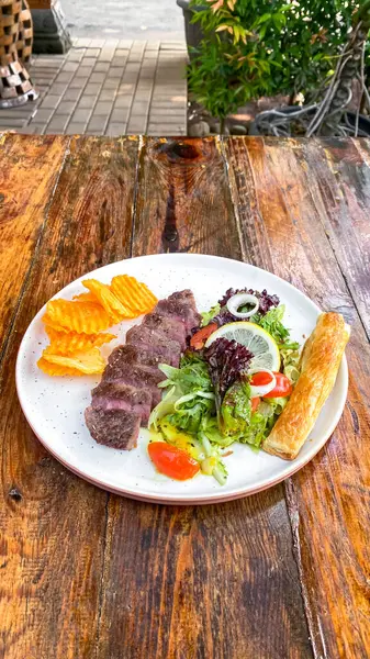 Sebzeli ızgara somon bifteği ve ahşap masada salata.