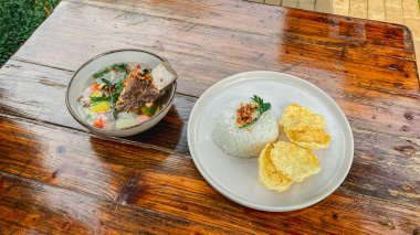 Bir kase pirinç, kızarmış domuz, sebze ve ahşap masada sos.