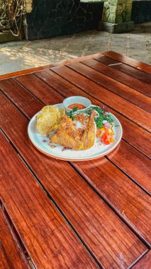 Tavuklu tavuk ve pilav. Tahta masadaki beyaz tabakta salata ile servis ediliyor.