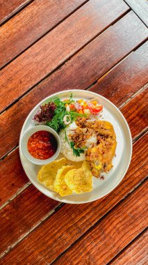 Endonezya yemeği: Kızarmış pirinç, kızarmış tavuk, kızarmış tavuk, ahşap arka planda beyaz bir tabakta yumurta ve sebze..