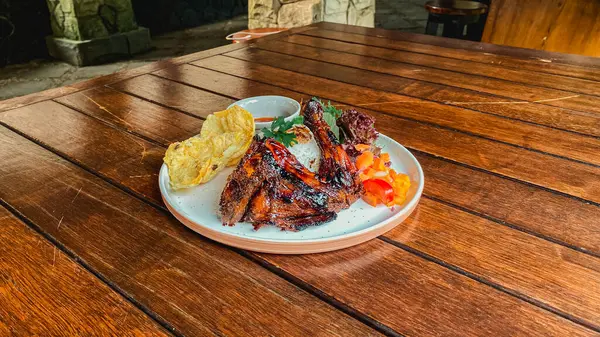 Tahta bir tabakta çatal ve sosla ızgara tavuk ve sebzelerden oluşan yüksek açılı bir çekim.