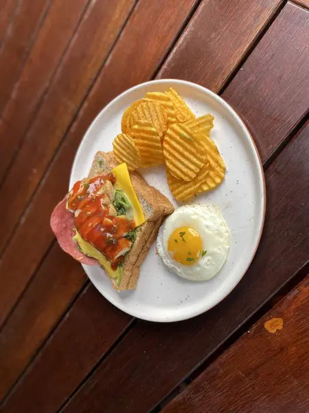 Tavuklu, peynirli, domatesli ve beyaz tabakta kızarmış yumurtalı sandviç.