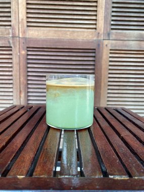 Bir bardak buzlu su ve ahşap zemin üzerinde yeşil yapraklar.