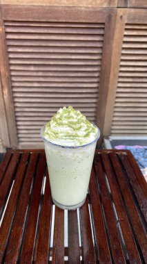 Bardakta kibrit yeşil çay, çırpılmış krema ve ahşap arka planda yeşil çay.