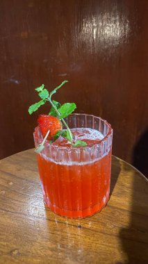 Bir bardak çilek suyu ve beyaz bir masada nane ve buz.