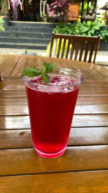 Ahşap masada bir bardak buz ve kırmızı kokteyl.