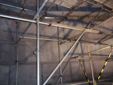 Beton bir duvara dayanan metal yapıları gösteren karmaşık bir iskelenin detaylı bir yakın çekimi. İnşaat, endüstri ve kentsel kalkınma temalarını gözler önüne serer.