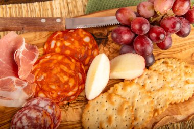 Kraker, üzüm ve elmalı ahşap bir tabak yemek. Krakerler tabağın sağ tarafında, üzümler ve elmalar da sol tarafında.