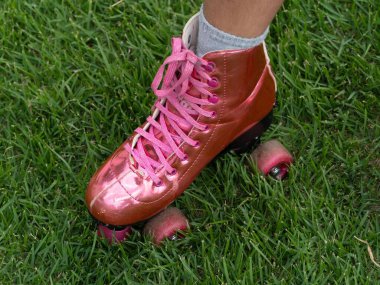 Bir çift parlak pembe paten ve bir kişi tarafından giyilen pembe bağcıklı yeşil çimenlerin üzerinde açık hava eğlencesi ve eğlenceli bir nostalji hissi taşıyan yakın plan bir fotoğraf..