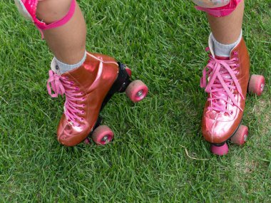 Yakından çekilmiş bir görüntü, bir kişi tarafından giyilen canlı pembe paten çifti gösteriyor, yemyeşil çimenlerin üzerinde duruyor, dışarıda eğlenceli ve eğlenceli bir eğlence atmosferi yakalıyor..