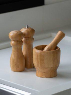 Estetik ahşap mutfak aletleri, biber öğütücü, tuzluk ve beyaz bir tezgahın üzerinde tokmak. Gösterişli ve modern mutfak eşyaları tasarımı sürdürülebilirliği ve işlevselliği vurguluyor.