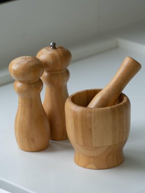 Estetik ahşap mutfak aletleri, biber öğütücü, tuzluk ve beyaz bir tezgahın üzerinde tokmak. Gösterişli ve modern mutfak eşyaları tasarımı sürdürülebilirliği ve işlevselliği vurguluyor.