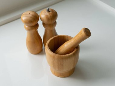 Estetik ahşap mutfak aletleri, biber öğütücü, tuzluk ve beyaz bir tezgahın üzerinde tokmak. Gösterişli ve modern mutfak eşyaları tasarımı sürdürülebilirliği ve işlevselliği vurguluyor.