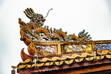 Hue, Vietnam 'daki tarihi bir binanın çatısındaki süslü ejderha oymalarının detaylı görüntüsü. Canlı renkler ve karmaşık detaylar geleneksel Vietnam mimarisi ve sanatını gözler önüne seriyor..