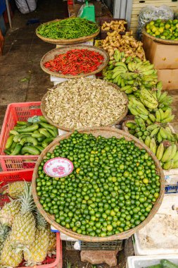 Hue, Vietnam 'da canlı bir piyasa sahnesi, dokunmuş sepetlerde çeşitli taze ürünler sergileniyor. Muz, salatalık ve kırmızı biber gibi diğer meyve ve sebzelerle çevrili yeşil kumkatlarla dolu büyük bir sepet taşar. Piyasa atmosferi 