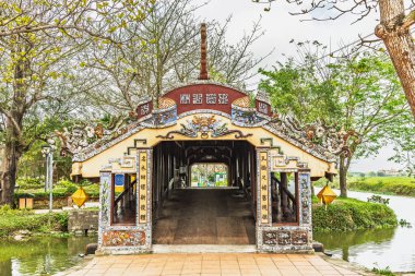 Hue, Vietnam 'daki canlı, süslü Thanh Toan Köprüsü sakin bir kanalda gururla duruyor. Köprünün karmaşık oymaları ve renkli ayrıntıları yemyeşil bir zemin ve berrak bir gökyüzüne vurgulandı..