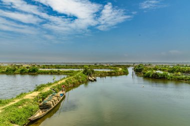 Hue, Vietnam 'da bir su yolu manzarası. Geleneksel ahşap botlar yemyeşil suların sakin kıyılarında, yemyeşil bitki örtüsüyle çevrili. Su yolu boyunca dar bir patika var. Huzurlu ve resimli bir manzara yaratıyor..
